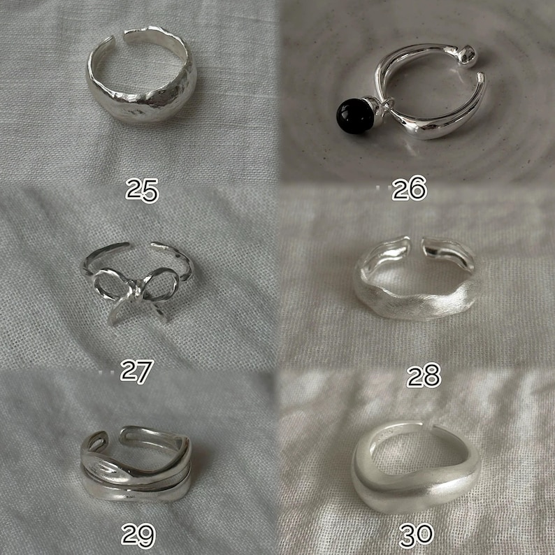 May include: A collection of silver rings in various designs. One ring has a textured surface, another features a bow, and a third has a black bead. Each ring is displayed on a neutral fabric background. Numbers 25, 26, 27, 28, 29, and 30 are visible.