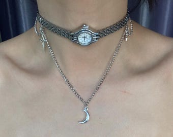 May include: A silver watch choker necklace with a crescent moon pendant on a silver chain.