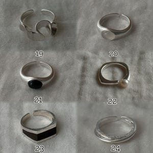 May include: A collection of silver rings, each with a unique design. One ring features an abstract shape, another has a rounded stone, and a third has a black stone. Other rings include a pearl and a geometric design. Numbers 19, 20, 21, 22, 23, and 24 are visible.