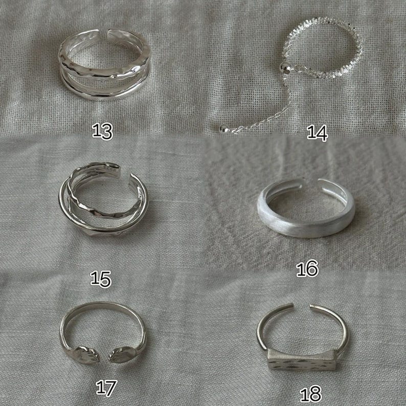 May include: A collection of silver rings, each with a unique design. The rings include adjustable styles, textured bands, and open designs. The image shows rings labeled 13, 14, 15, 16, 17, and 18. The rings are displayed on a neutral fabric background.