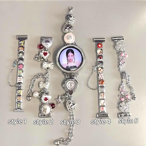 May include: A collection of five decorative watch bands and a smartwatch. The bands are silver-toned and adorned with charms, including hearts, bows, and small images. The smartwatch displays a photo of a person on its screen.