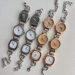 Puede incluir: Cuatro pulseras de reloj plateadas y doradas. Cada pulsera presenta una serie de esferas de reloj de formas cuadradas y redondas. Las esferas tienen esferas blancas, negras y doradas con números romanos y arábigos. Las pulseras tienen eslabones de cadena y cierres de mosquetón.