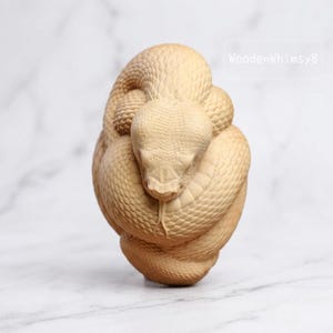 May include: A detailed wooden sculpture of a coiled snake, showcasing intricate scale patterns and a focused gaze. The snake's head is prominently displayed, with its forked tongue extended. The sculpture is a natural wood color.