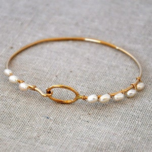 May include: A gold bangle bracelet with a simple oval clasp and freshwater pearls strung along the wire.