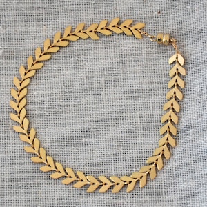 May include: A gold chevron bracelet with a matte finish. The bracelet is made of small, linked, arrow-shaped pieces.