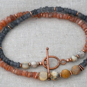 May include: A necklace made with sunstone, iolite, and copper beads. The necklace has a copper clasp.