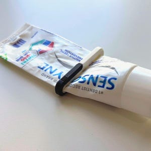 May include: A white and blue tube of Sensodyne toothpaste with a black and white tube squeezer. The tube squeezer is designed to help dispense the toothpaste. The text on the tube reads "Sensitivity Gum Enamel".