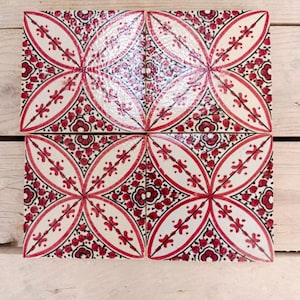 Könnte beinhalten: Vier quadratische Keramikfliesen, die zusammen angeordnet sind und ein sich wiederholendes Blumenmuster aufweisen. Das Design umfasst rote und schwarze Akzente auf weißem Hintergrund und erzeugt ein symmetrisches, dekoratives Motiv. Die Fliesen sind für die Inneneinrichtung geeignet.