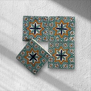 Può includere: Quattro piastrelle quadrate in ceramica con sfondo turchese e un motivo a stella ripetuto in arancione, bianco e blu navy. Una piastrella è angolata, mostrando il lato.