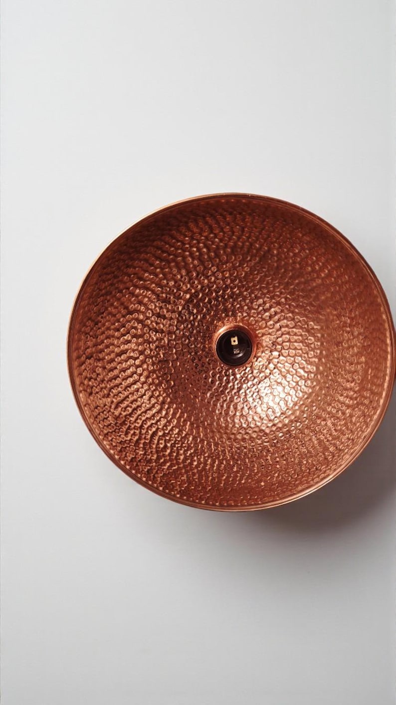May include: A copper-colored, hammered metal bowl with a textured surface. The bowl has a rounded shape and a small, dark center. The bowl is likely used for decorative or functional purposes.