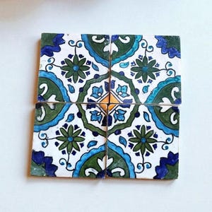 Peut inclure: Quatre carreaux de céramique carrés, disposés ensemble, avec un motif floral répété dans les tons de vert, de bleu et de blanc. Le motif comprend des fleurs stylisées et des lignes courbes, avec un accent jaune central. Les carreaux sont probablement pour la décoration intérieure.