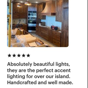 May include: A kitchen with wooden cabinets, a range, and a copper range hood. Three copper pendant lights hang above the island. The text says, "Absolutely beautiful lights, they are the perfect accent lighting for over our island. Handcrafted and well made."