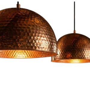 May include: Three copper pendant lights with a hammered texture and a warm, golden interior. The dome-shaped shades hang from black cords, creating a modern and stylish lighting fixture. The copper finish adds a touch of elegance.