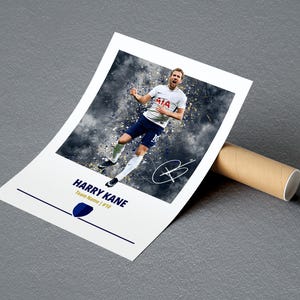 K&ouml;nnte beinhalten: Ein wei&szlig;-blaues Fu&szlig;balltrikot mit einem Spieler, der ein Tor feiert. Das Trikot tr&auml;gt den Text "AIA" auf der Vorderseite und die Nummer "10" auf der R&uuml;ckseite. Der Spieler ist Harry Kane, und der Text "HARRY KANE Team Name | #10" befindet sich unter dem Bild.