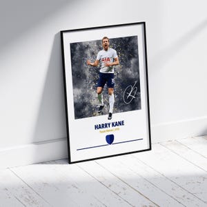 K&ouml;nnte beinhalten: Ein gerahmtes Poster mit einem Fu&szlig;ballspieler in einem wei&szlig;en Trikot mit einem blau-wei&szlig;en Logo. Der Spieler springt mit erhobenen Armen in die Luft. Der Hintergrund ist ein verschwommenes Bild eines Fu&szlig;ballfeldes. Das Poster hat einen schwarzen Rahmen und der Name des Spielers, "HARRY KANE", ist in goldenen Buchstaben unter dem Bild gedruckt. Der Text "Team Name | #10" ist in schwarzen Buchstaben unter dem Namen des Spielers gedruckt.