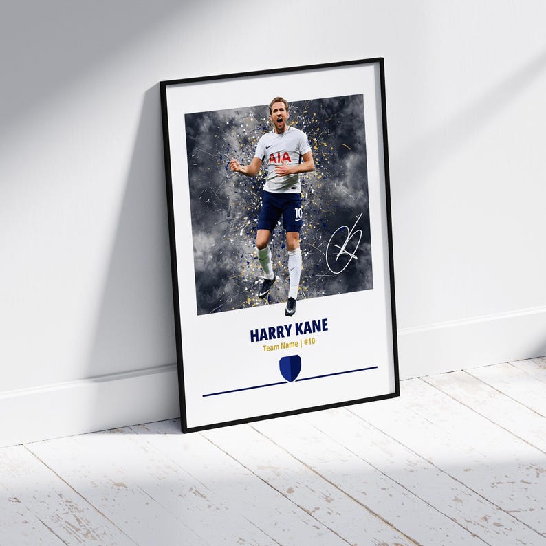 K&ouml;nnte beinhalten: Ein gerahmtes Poster mit einem Fu&szlig;ballspieler in einem wei&szlig;en Trikot mit einem blau-wei&szlig;en Logo. Der Spieler springt mit erhobenen Armen in die Luft. Der Hintergrund ist ein verschwommenes Bild eines Fu&szlig;ballfeldes. Das Poster hat einen schwarzen Rahmen und der Name des Spielers, "HARRY KANE", ist in goldenen Buchstaben unter dem Bild gedruckt. Der Text "Team Name | #10" ist in schwarzen Buchstaben unter dem Namen des Spielers gedruckt.