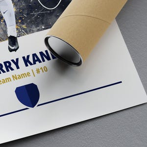 K&ouml;nnte beinhalten: Ein wei&szlig;-blaues Poster mit einer Aquarell-Illustration eines Fu&szlig;ballspielers. Das Poster tr&auml;gt den Text "HARRY KANE" und "Team Name | #10" in goldenen Buchstaben. Unter dem Text befindet sich ein blaues Schildlogo.