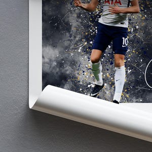 K&ouml;nnte beinhalten: Ein Fu&szlig;ballspieler in einem wei&szlig;en und blauen Trikot mit der Nummer 10 auf dem R&uuml;cken, der einen Fu&szlig;ball tritt. Der Hintergrund ist dunkelblau mit wei&szlig;en und goldenen Spritzern.