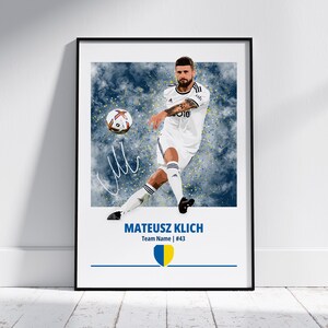 May include: Framed print featuring a soccer player in a white uniform kicking a soccer ball. The print includes the player's name, team information, and a signature. The background is a blue and white abstract design.