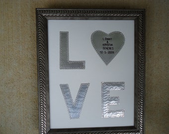 May include: A framed metal art piece with the word "LOVE" spelled out in large silver letters. The letters are decorated with silver rivets. A silver heart with the text "Lonny & Krystin Sekeres 12-5-2009" is above the letters.