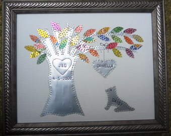 Puede incluir: Un árbol de metal plateado con hojas de colores y un corazón con las iniciales "J&D" y la fecha "4-5-2009". Un corazón más pequeño con el nombre "Daniella" cuelga de una rama. Un perro de metal plateado con el nombre "Daisy" está debajo del árbol.