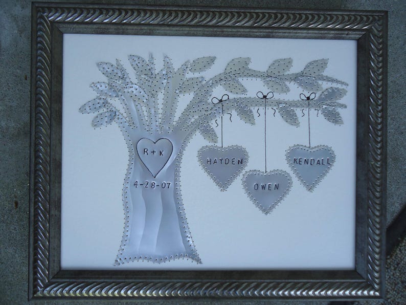 Puede incluir: Una imagen enmarcada en metal plateado con un fondo blanco que presenta un &aacute;rbol con corazones colgando de las ramas. El tronco del &aacute;rbol tiene las iniciales "R+K" y la fecha "4-28-07" inscritas. Los corazones tienen los nombres "Hayden", "Owen" y "Kendall" inscritos.