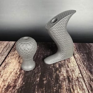 May include: Two dark grey metal objects with a textured, geometric diamond pattern. One object is a rounded, bulbous shape with a flat base and a circular opening at the top. The other is a curved, boot-like shape with a flat base and a top opening.