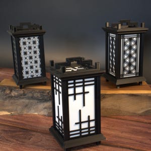 May include: Three black wooden lanterns with different geometric patterns. The lanterns are on a wooden surface.