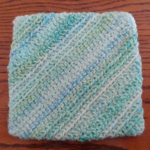 May include: A square crocheted dishcloth in shades of blue, green, and white. The cloth has a diagonal pattern.