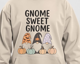 May include: Beige hoodie with the text "Gnome Sweet Gnome" in black. The design features three gnomes with pumpkin and fall-themed hats and pumpkins. The hoodie has a front pocket and a drawstring hood.