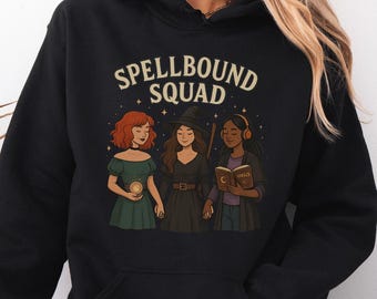 May include: Black hooded sweatshirt with the text "SPELLBOUND SQUAD" above a graphic of three women. One woman has red hair and holds a glowing orb, another wears a witch hat, and the third wears headphones and holds a book.