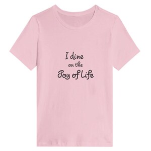 May include: A pink t-shirt with the text "I dine on the Joy of Life" printed in black.