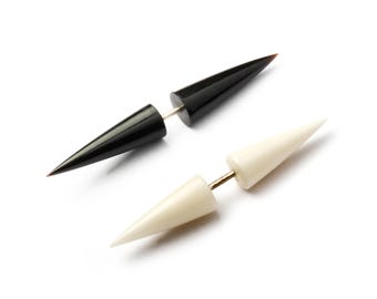 Könnte beinhalten: Ein Paar schwarze und weiße spitze Ohrstecker. Die Stecker sind aus einem glatten, polierten Material gefertigt und haben eine scharfe, spitze Spitze.