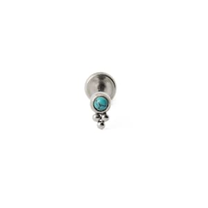 May include: A silver lip piercing featuring a turquoise stone and three small silver beads. The piercing has a flat back and a decorative front. The turquoise stone is round and set in a silver bezel. The three beads are arranged in a triangular pattern.