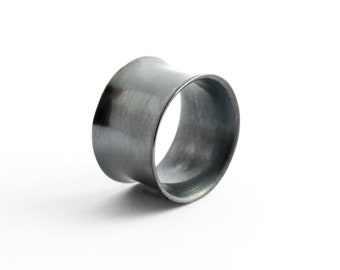 May include: A dark gray metal ear gauge tunnel with a smooth, brushed finish. The jewelry features a concave, flared shape that is wider at the edges and tapers toward the center, creating a hollow, cylindrical opening for body modification.
