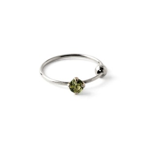 Peut inclure: Une bague en argent avec une petite pierre précieuse verte. La bague est de style cerceau avec une boule à l'extrémité.