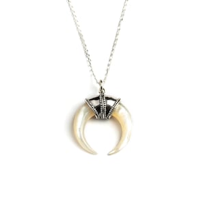 Peut inclure: Un collier en chaîne argent avec un pendentif en forme de croissant de lune blanc. Le pendentif est en nacre et a une bordure argentée.