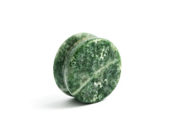 Puede incluir: Un expansor de oreja circular con un patrón de piedra moteado en verde bosque y blanco. La pieza de joyería tiene una superficie lisa y pulida con una sección central cóncava distintiva y bordes planos y redondeados en ambos lados.