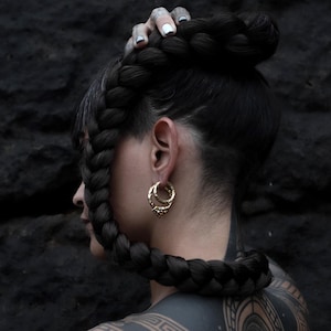 Pode incluir: Uma pessoa com cabelo comprido e preto trançado, usando um par de brincos de argola de ouro com uma superfície texturizada.