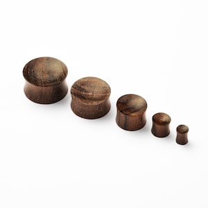 May include: Set of five wooden ear gauges in various sizes. The gauges are dark brown with a natural wood grain pattern.