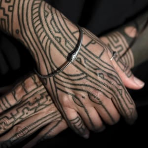 Puede incluir: Primer plano de las manos de una persona con intrincados tatuajes geométricos negros. La persona lleva una fina pulsera de plata en la muñeca.