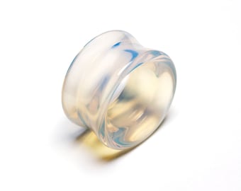 May include: A translucent, wide-band ring crafted from smooth, polished material. The ring features a milky, opalescent appearance with subtle swirls of pale blue and warm yellow tones visible throughout its curved, cylindrical structure.