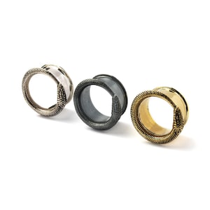 May include: Three circular ear tunnels arranged in a row, each featuring a textured snake design wrapping around the front edge. The tunnels are finished in silver, matte black, and gold tones, showcasing detailed scale patterns on the snake bodies.