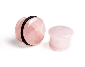 May include: Two circular ear plugs crafted from smooth, polished light pink stone. One plug features a thin black rubber O-ring encircling its side, while the other is a solid, smooth-surfaced piece with a slightly flared edge design.