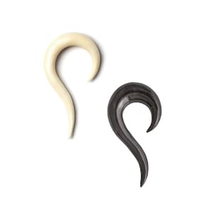 Puede incluir: Dos expansores de oreja, uno negro y uno blanco, en forma de gancho curvo.