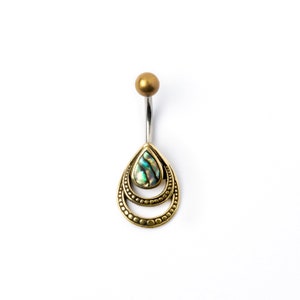 Peut inclure: Un piercing de nombril avec un dessus doré et une barre incurvée argentée. Le pendentif présente une forme de goutte d'eau avec un cadre doré et un centre nacré et irisé. Le cadre a un motif pointillé.