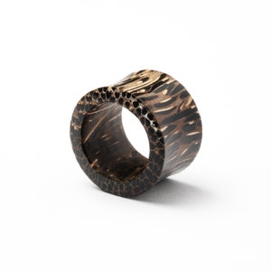 May include: A black and brown wooden ring with a patterned design. The ring is made of natural wood and has a unique, organic look.