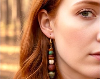 May include: A close-up of a woman with red hair wearing a long, dangling earring. The earring features a gold hook and a series of beads in various colors, including brown, green, white, and red. The beads are stacked, creating a layered effect.