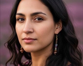 May include: A portrait of a person with dark hair and brown eyes, wearing ornate earrings and a purple embroidered top. The background is a soft, blurred field of purple.