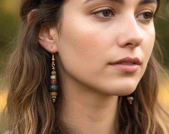 May include: A close-up of a person wearing long, dangling earrings. The earrings feature a gold-colored hook and a series of colorful, rounded beads in shades of brown, green, and red. The person has long, wavy brown hair.